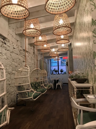 The interior of Lov, with whitewashed brick walls, hanging wicker chairs, and rattan light fixtures.